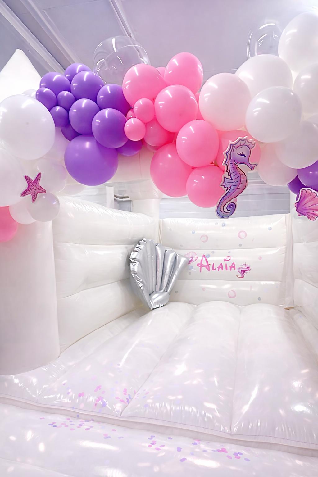 White mermaid bouncy castle with purple and pink balloon garland